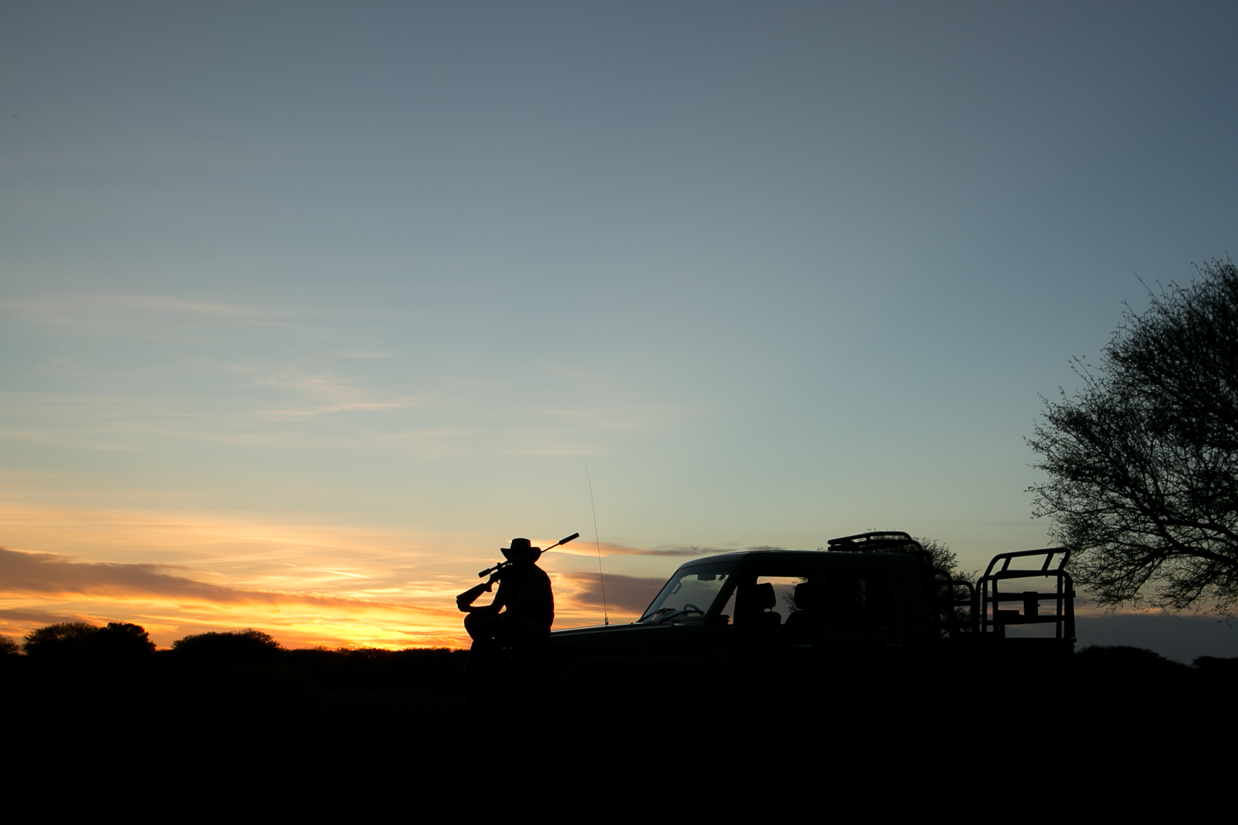 A person sitting on a safari vehicle with a rifle