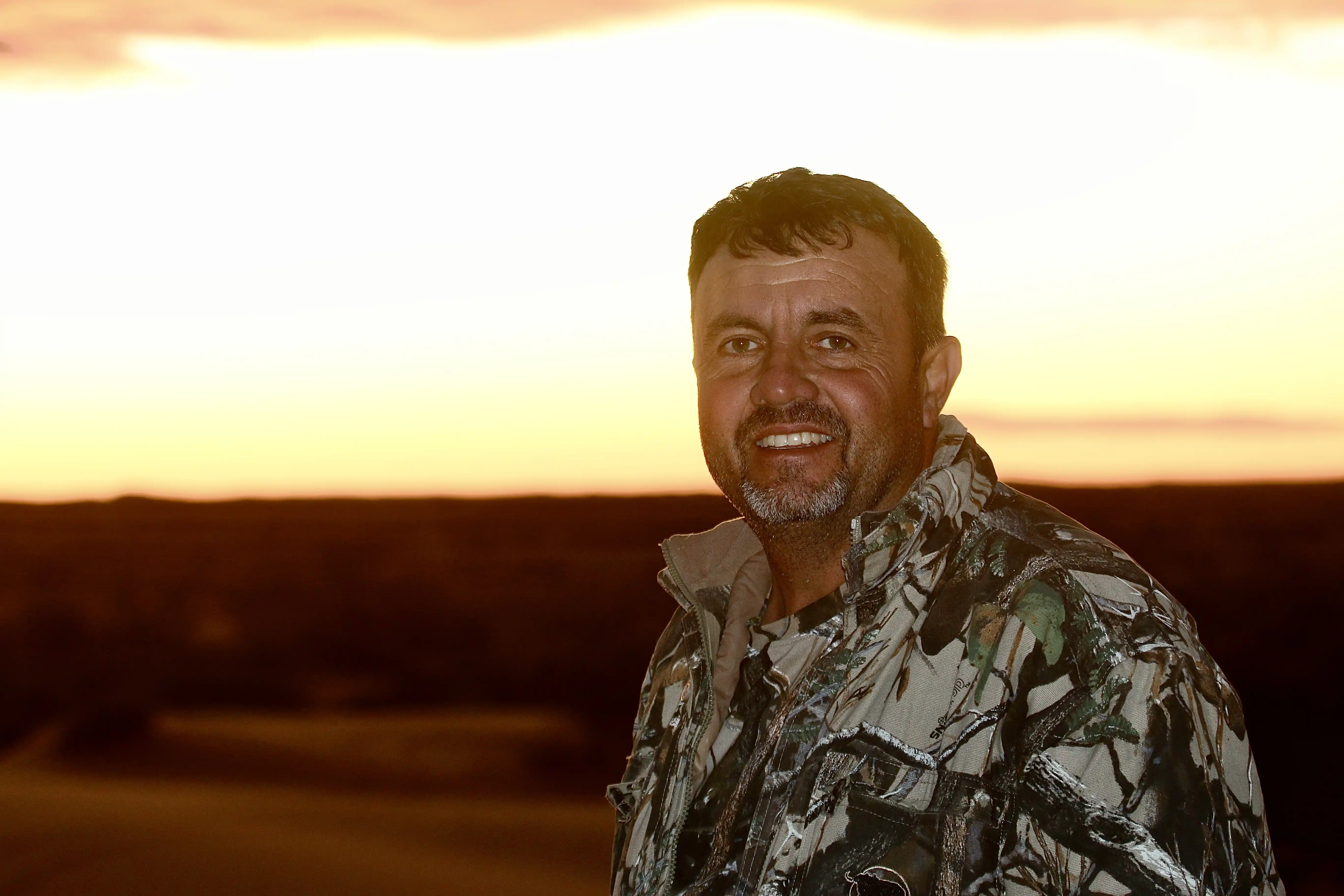 A man in hunting camouflage against a beautiful African sunset
