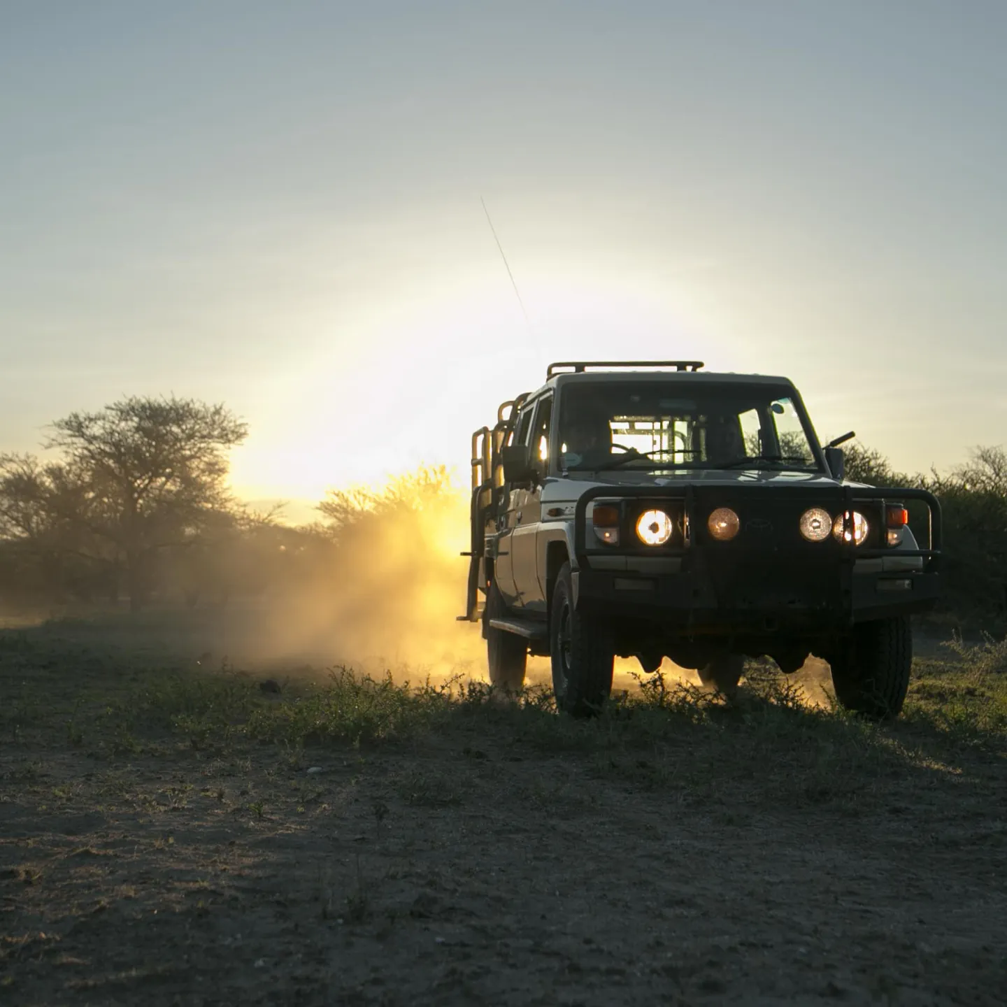 Beige safari vehicle parked on a dirt road near a water body